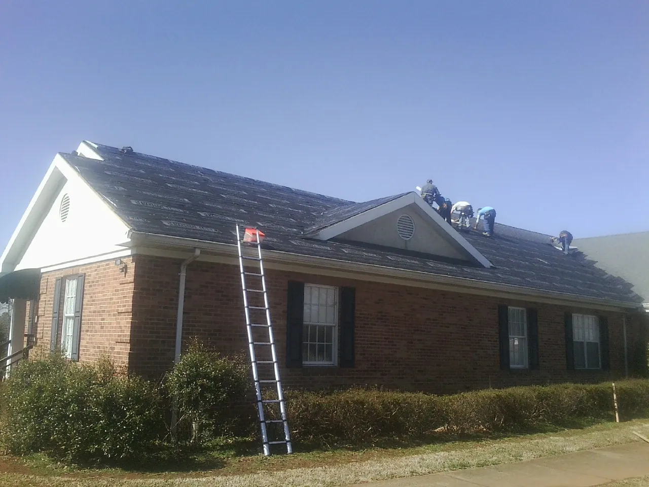 Crew tearing shingles off a brick ranch roof with a ladder set — Metal Roof Repair work by our crew in East Dennis