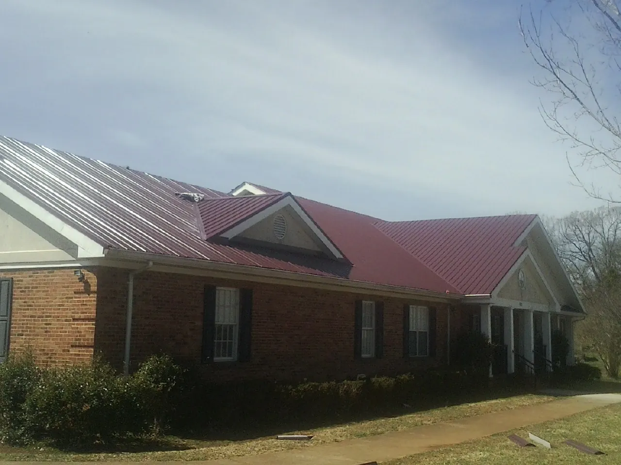 Red metal roof with gabled entries on a long brick building, from a Hail Damage Roof Repair job in East Dennis