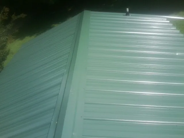 New green metal panels meeting at the ridge of a roof — Flat Roof Repair work by our crew in East Dennis