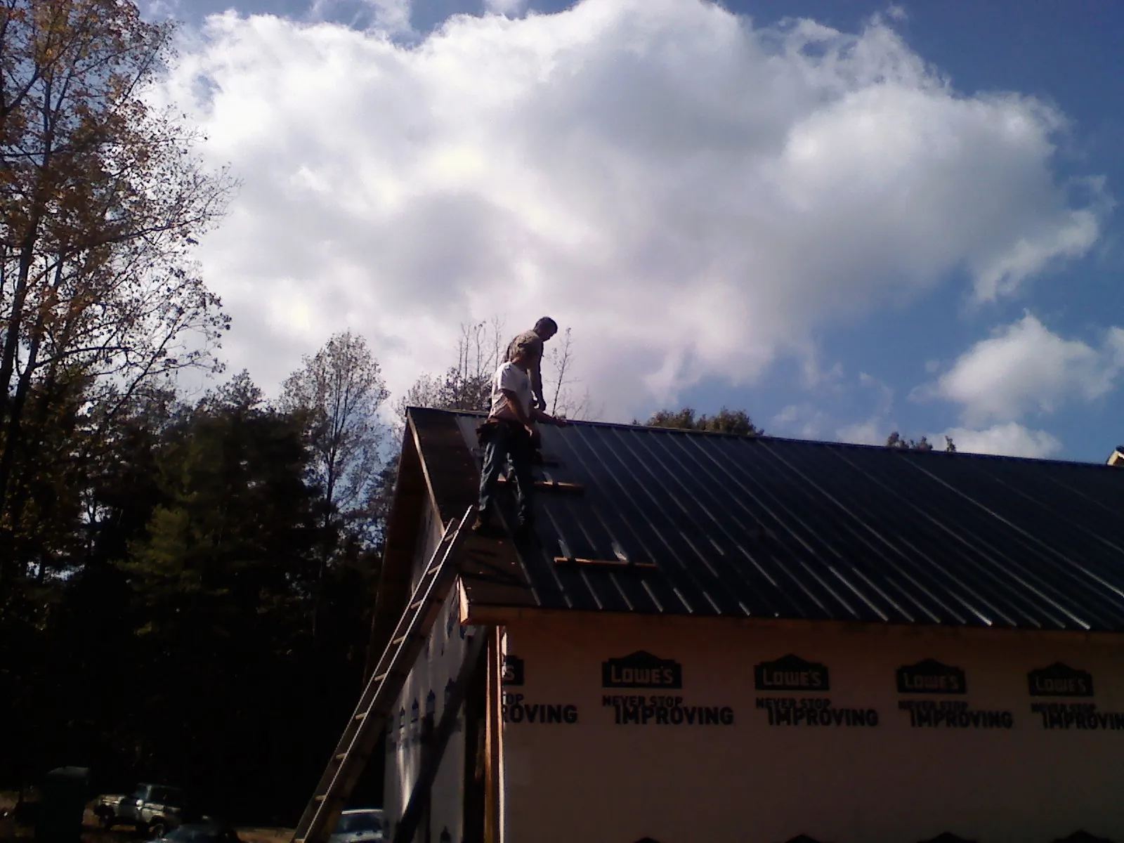 Roofer fastening dark metal panels high against a cloudy sky, from a Roof Inspection job in East Dennis