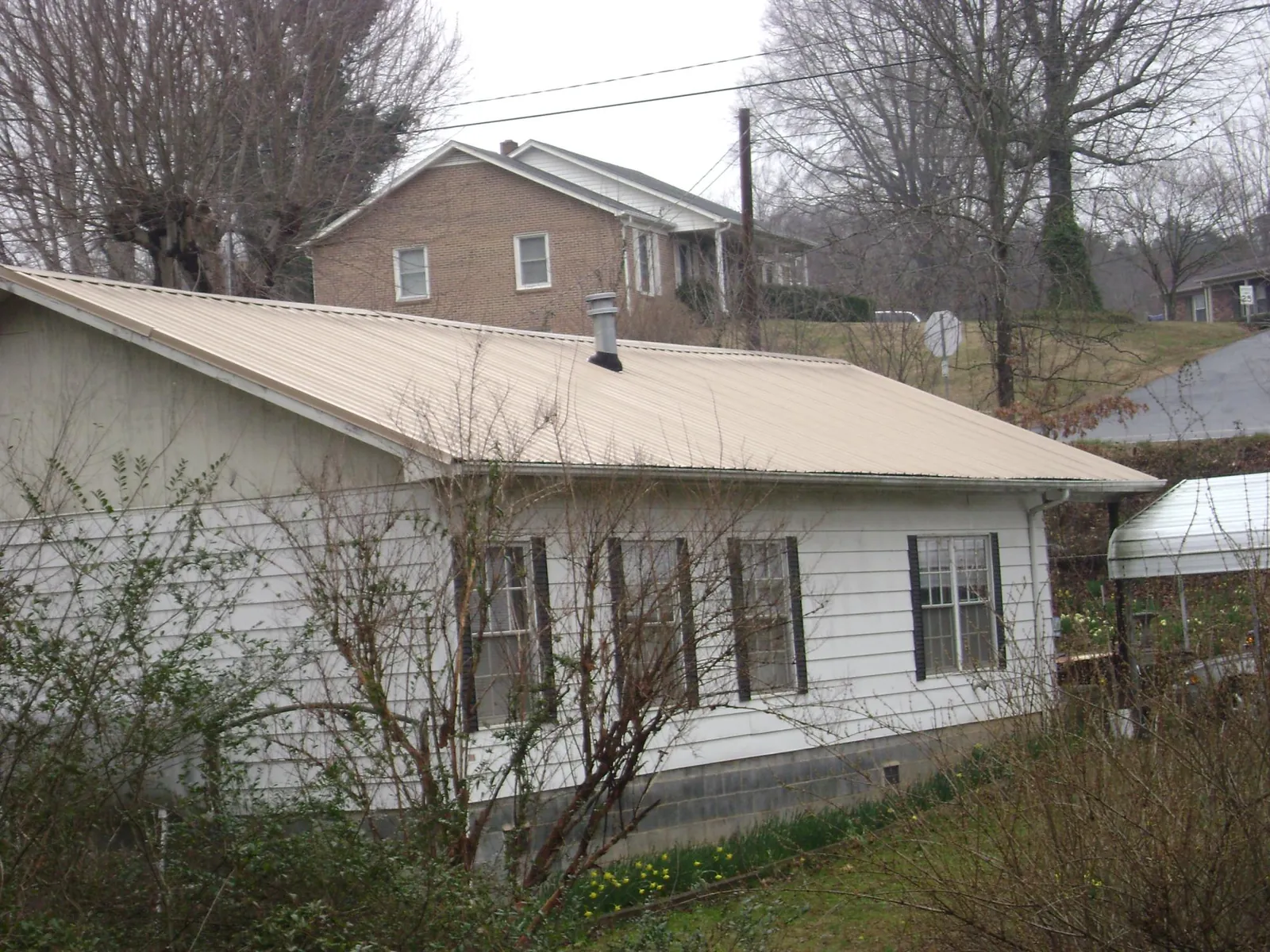 Tan metal roof on a white sided house set into a hillside — Commercial Roofing by Roofing Brothers in East Dennis
